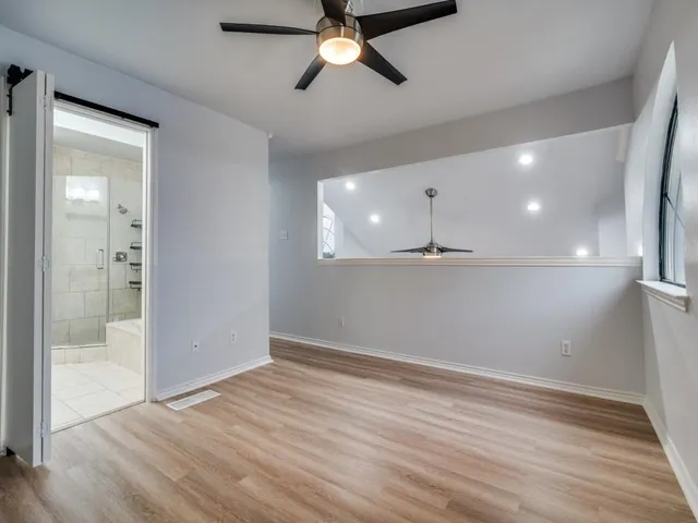 an empty room with wooden floor a ceiling fan and windows