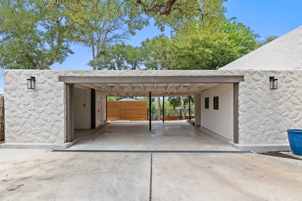 716 North Commons Ford Road Austin, TX 78733 - Photo 29 of 30 Carport featuring a concrete driveway, textured stone-look exterior walls, and exposed wood beam ceiling