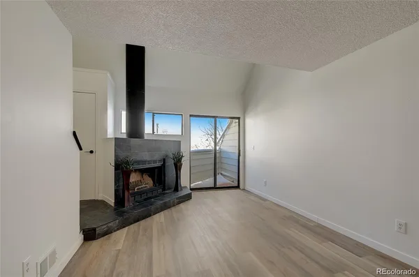 a view of an empty room with wooden floor fireplace and a window