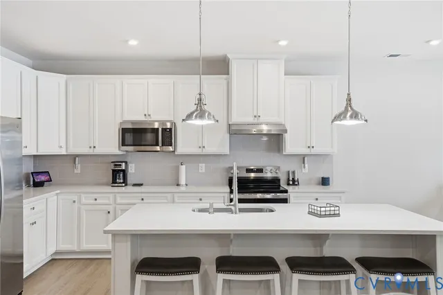a kitchen with stainless steel appliances a sink a stove a refrigerator cabinets and chairs