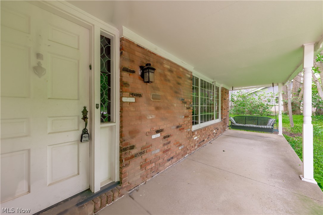 25001 Letchworth Road Beachwood, OH 44122 - Photo 43 of 50 Covered front porch featuring a white panel door with decorative sidelight, brick exterior, multiple pane windows, and a concrete floor