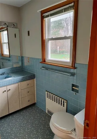 a bathroom with a granite countertop toilet a sink a mirror and a window