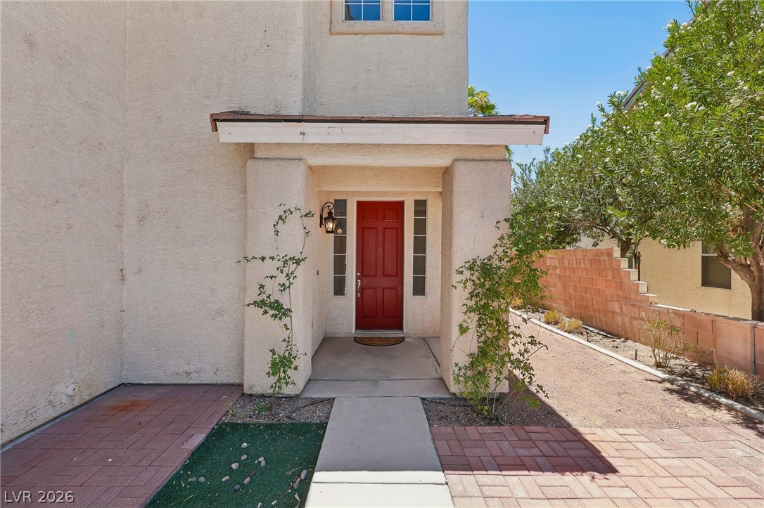 1727 Millstream Way Henderson, NV 89074 - Photo 9 of 46 A striking red door welcomes guests to this stucco home, framed by lush greenery and contrasting brick paving.