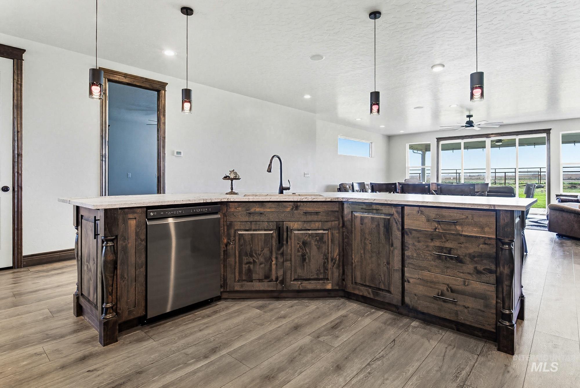 24753 Simplot Boulevard Wilder, ID 83676 - Photo 10 of 47 Kitchen with dark wood finish cabinetry, stainless steel dishwasher, pendant lighting, a center island with sink, and a textured ceiling