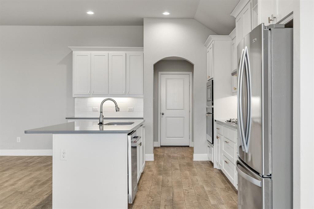 915 Timber Ridge Drive Justin, TX 76247 - Photo 10 of 39 Kitchen featuring wood-finish flooring, white shaker cabinetry, stainless steel appliances, a center island with a sink, and an arched doorway