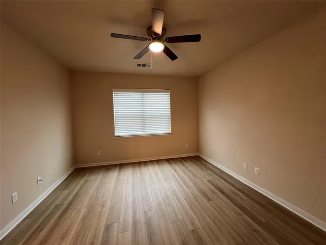 an empty room with wooden floor chandelier fan and windows