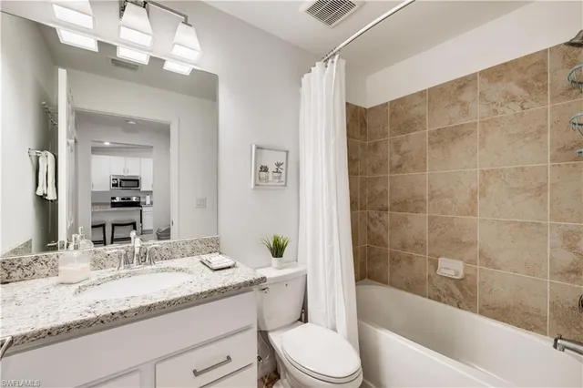 a bathroom with a granite countertop sink a toilet a mirror a bathtub and shower