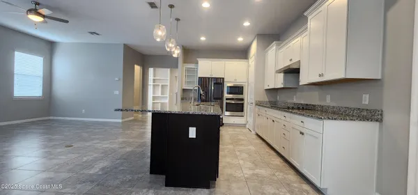 a large kitchen with kitchen island granite countertop a stove a sink a refrigerator and white cabinets with wooden floor