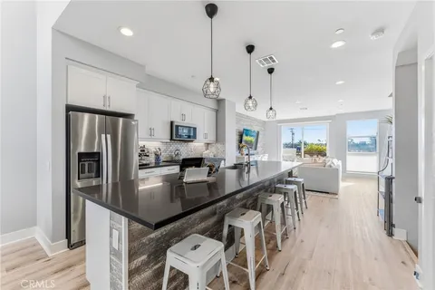 a kitchen with stainless steel appliances granite countertop a refrigerator a sink dishwasher a stove and a dining table with wooden floor