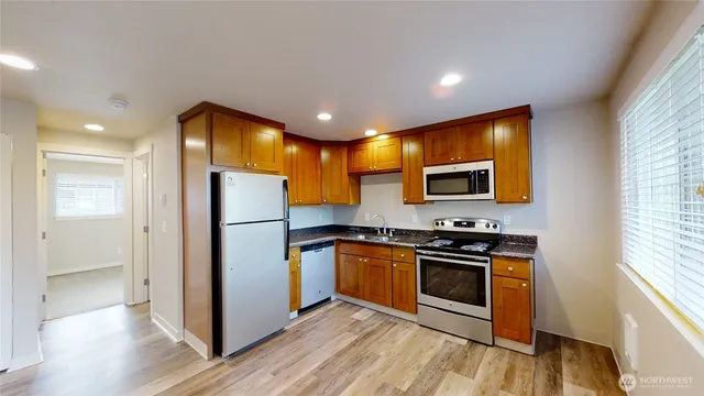 a kitchen with stainless steel appliances granite countertop a stove top oven a refrigerator a sink and dishwasher with wooden floor