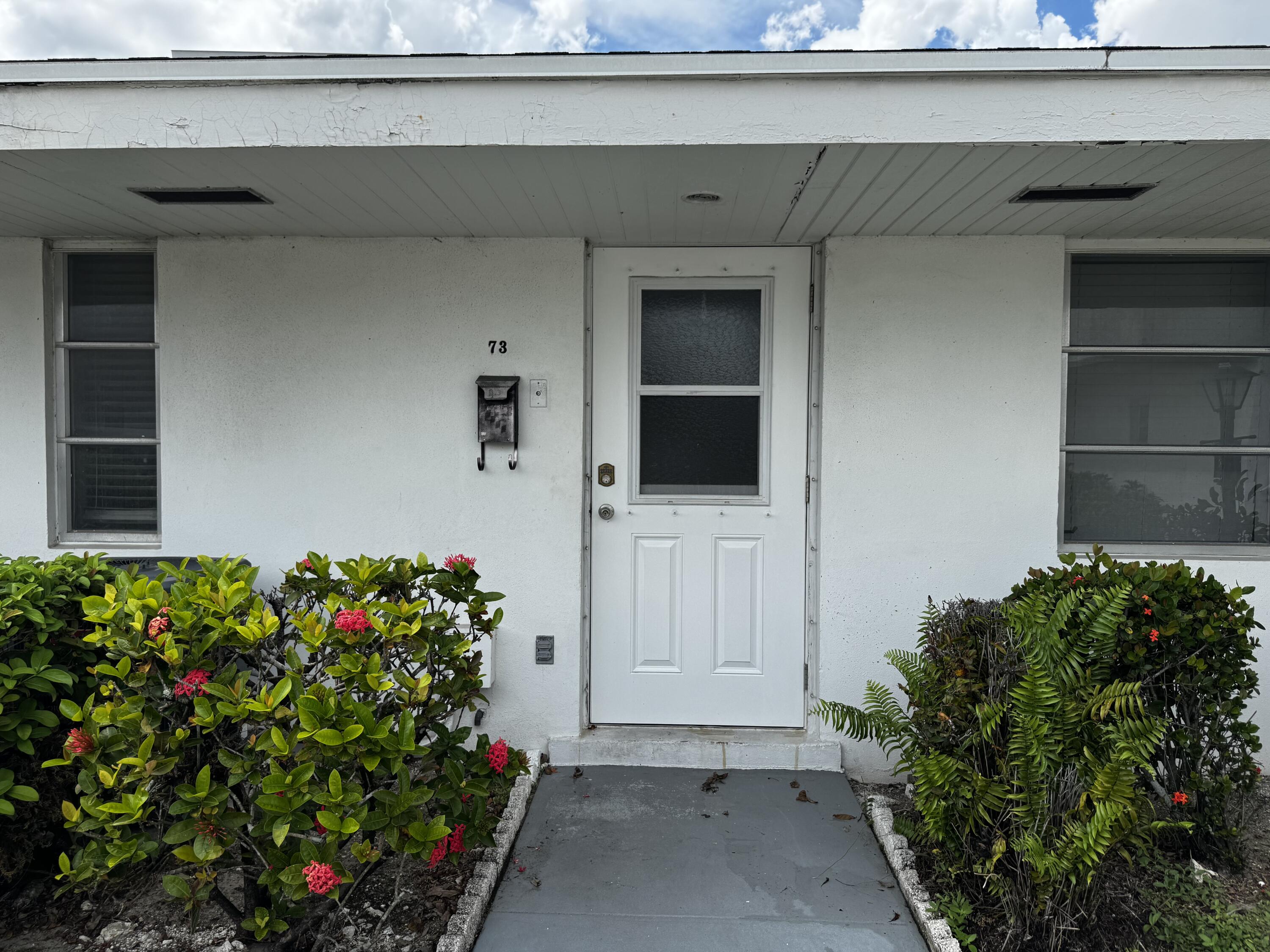 73 East Court, Unit 73 Royal Palm Beach, FL 33411 - Photo 1 of 17 a flower plants in front of a door