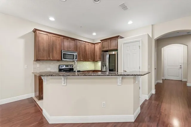 a kitchen with stainless steel appliances granite countertop wooden cabinets a refrigerator a sink a stove a microwave and wooden floors