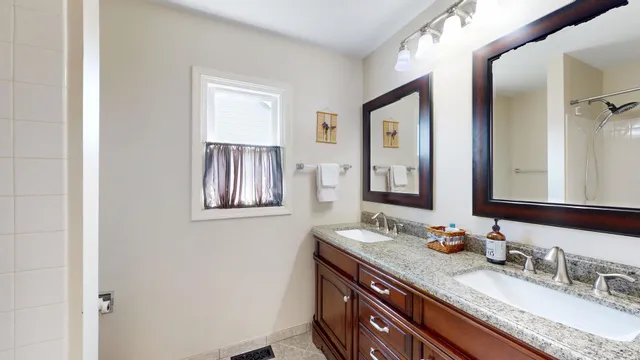 a bathroom with a granite countertop double vanity sink a mirror and window