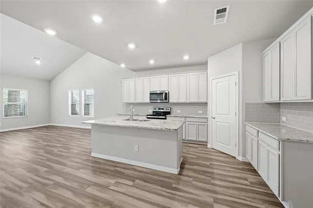 a kitchen with stainless steel appliances granite countertop a stove top oven a sink and white cabinets