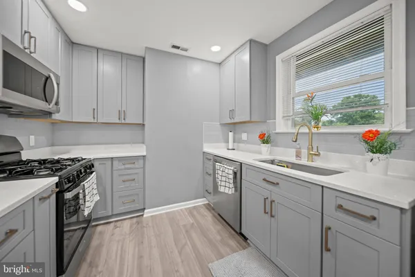 a kitchen with stainless steel appliances granite countertop white cabinets a sink a stove a window and wooden floor