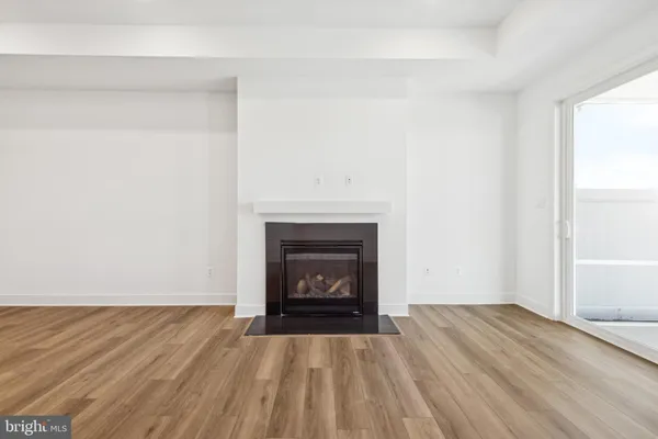 a view of an empty room with wooden floor fireplace and a window