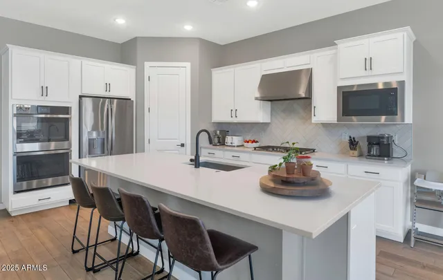 a large white kitchen with a stove a sink a refrigerator and white cabinets with wooden floor