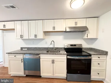 a kitchen with stainless steel appliances granite countertop a stove a sink and white cabinets