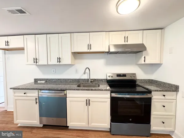a kitchen with stainless steel appliances granite countertop a stove a sink and white cabinets