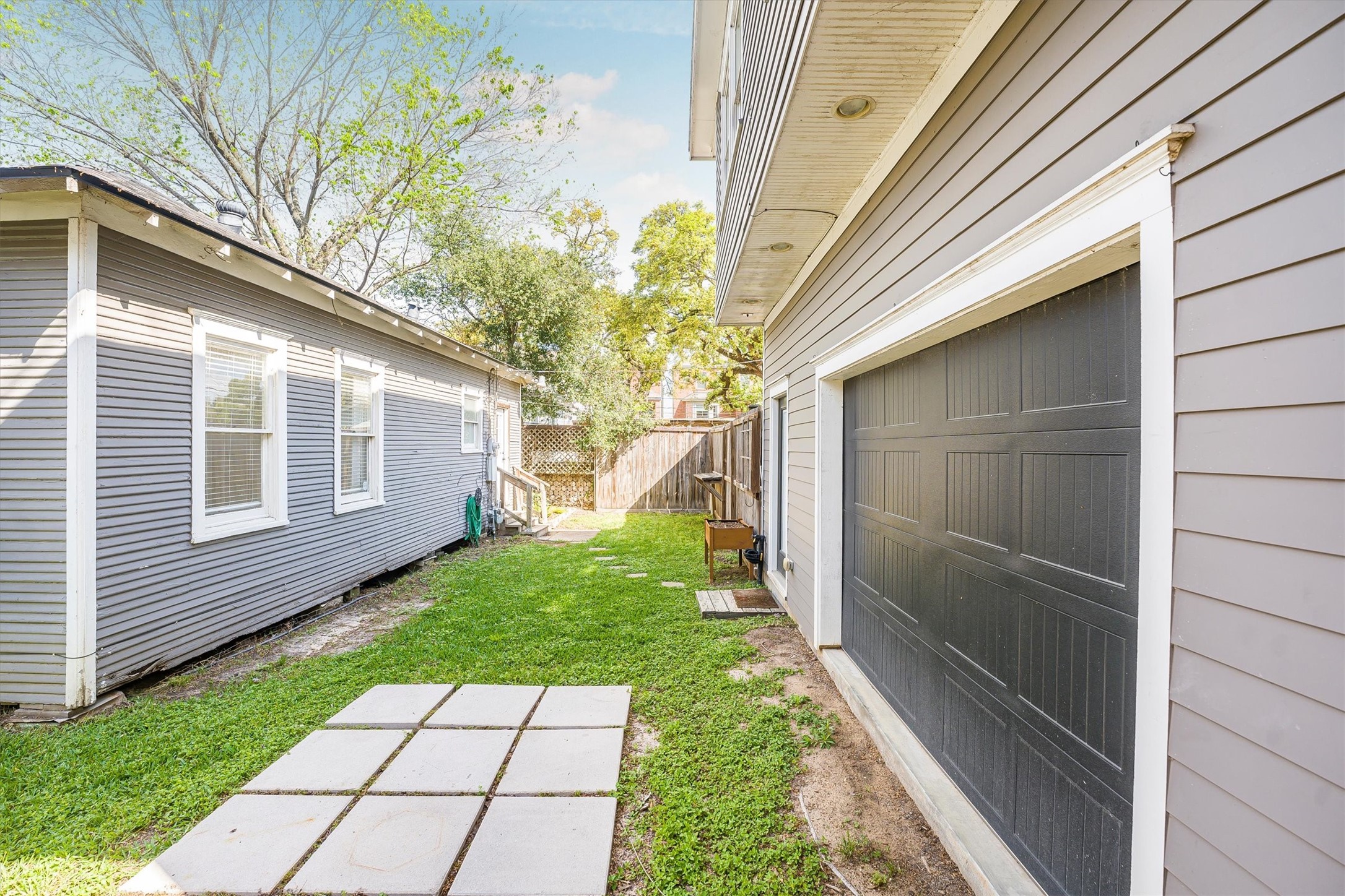 210 Tabor Street Houston, TX 77009 - Photo 12 of 18 The photo showcases a tidy backyard area. One side features garage/ garage apartment with a large black door, and the house has windows, creating a cozy and functional outdoor space.
