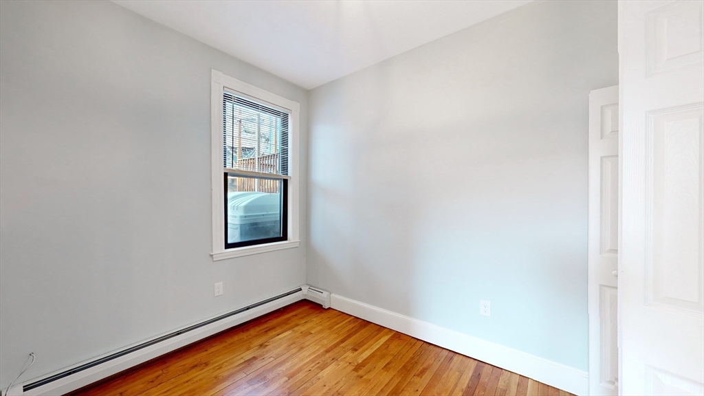 181 Highland Street, Unit 1 Boston, MA 02119 - Photo 7 of 11 a view of an empty room with wooden floor and a window