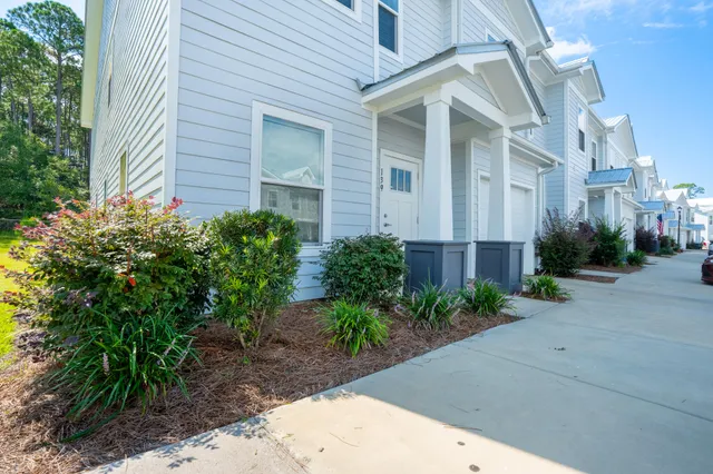 a view of a brick house with plants and large trees