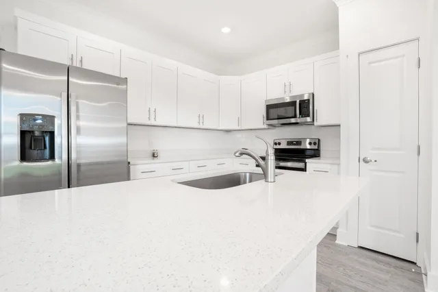 a kitchen with stainless steel appliances a refrigerator a sink a stove a microwave and white cabinets