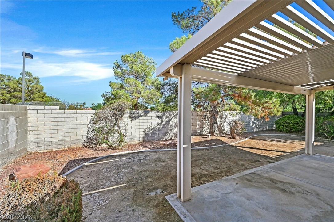 8830 Haviland Road Las Vegas, NV 89123 - Photo 27 of 43 A covered concrete patio overlooks a fenced backyard lined with mature trees.