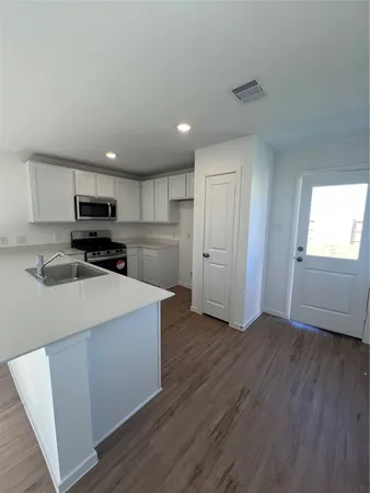 a kitchen with stainless steel appliances granite countertop a refrigerator a sink dishwasher a stove and white countertops with wooden floor