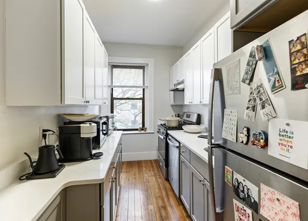 a kitchen with stainless steel appliances a stove a sink a refrigerator white cabinets and wooden floor
