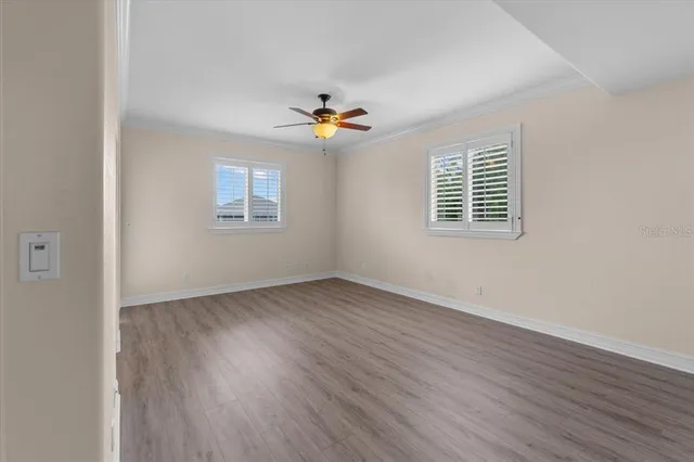 an empty room with wooden floor ceiling fan and windows