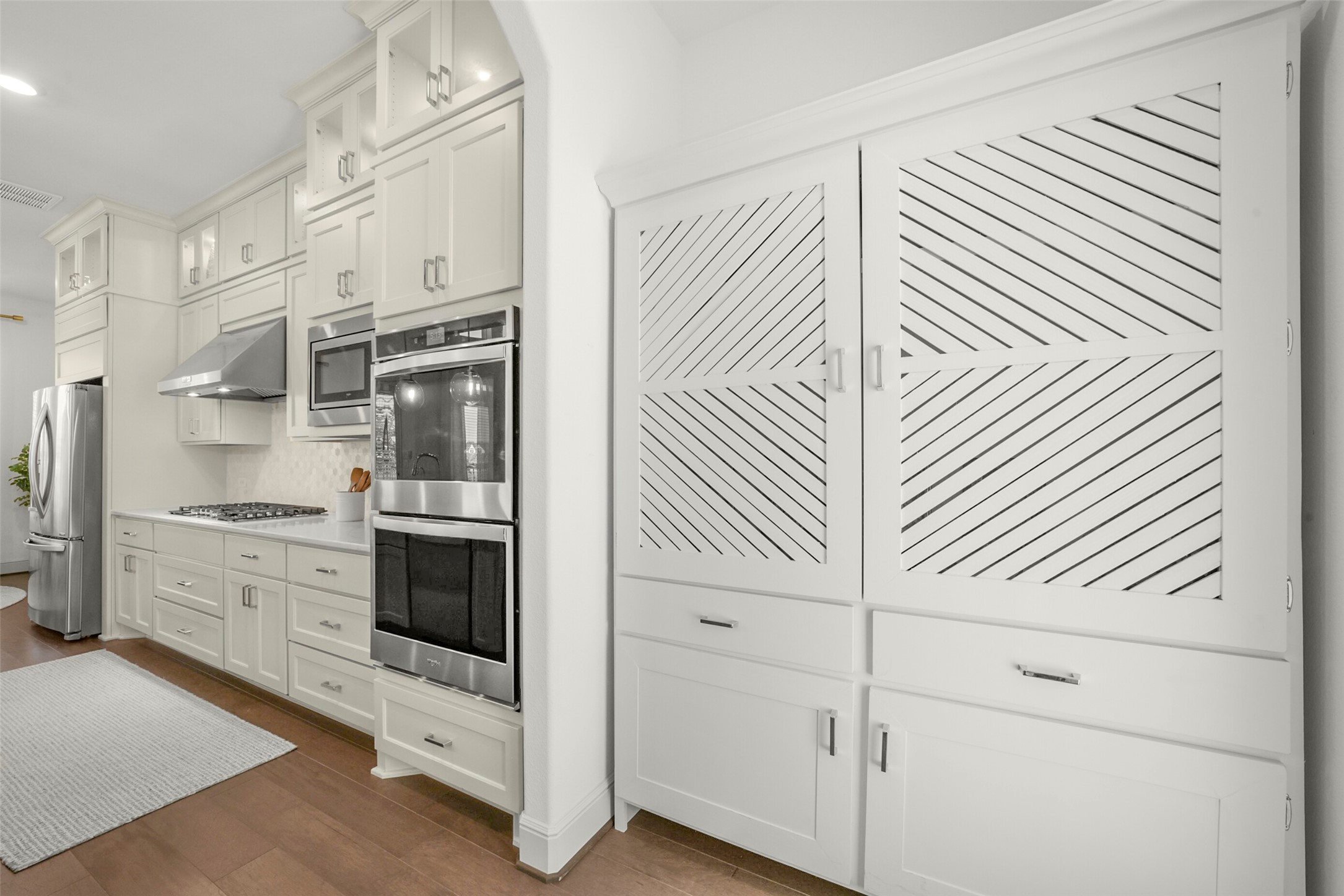 2018 Grove Terrace Lane Manvel, TX 77578 - Photo 11 of 50 This kitchen features modern white cabinetry, a stainless steel range hood, and double ovens. It includes a sleek refrigerator and ample storage with a stylish diagonal-patterned pantry. The space is bright and inviting with a classic, clean design.