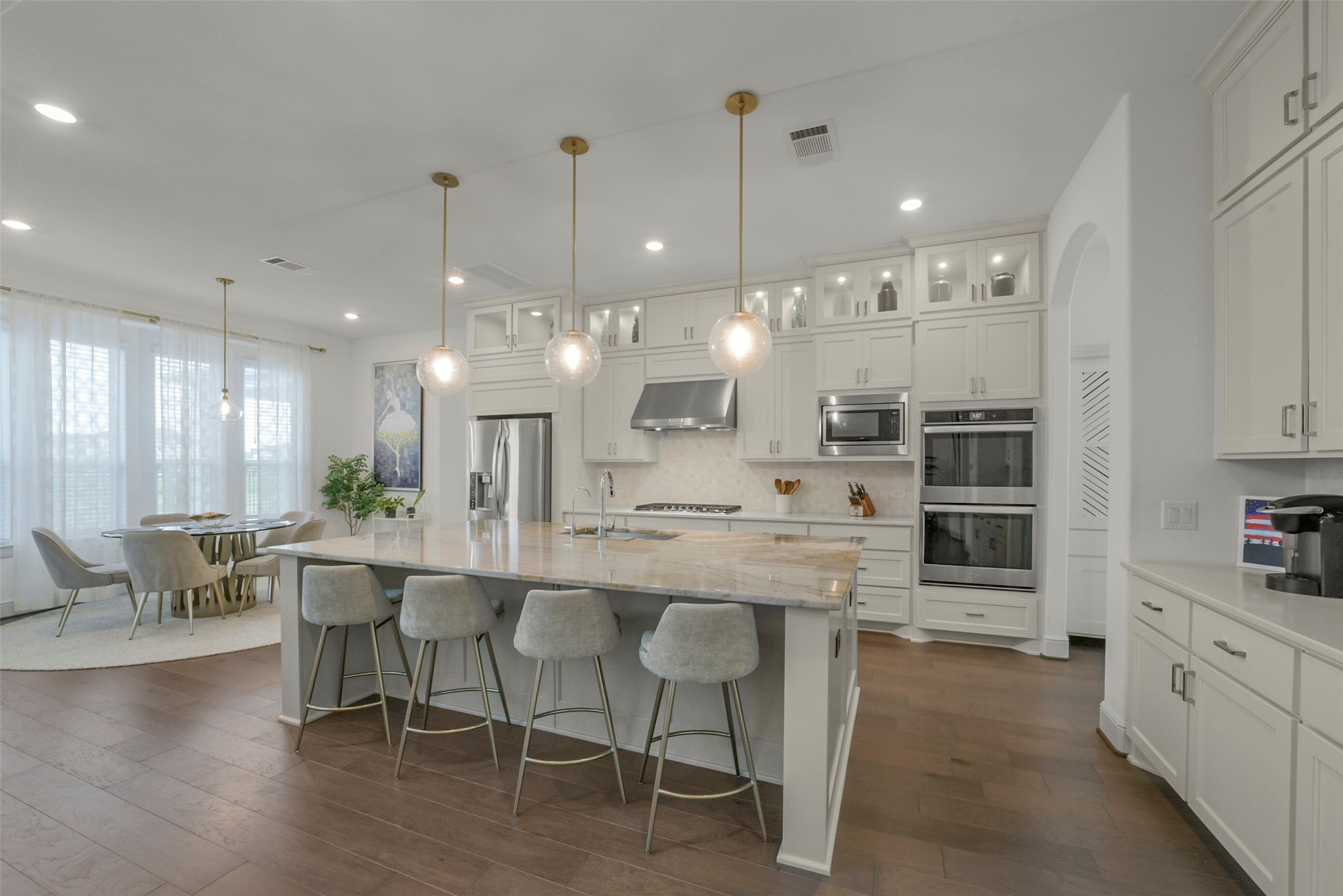 2018 Grove Terrace Lane Manvel, TX 77578 - Photo 14 of 50 Modern kitchen features a large island with seating, elegant pendant lighting, and stainless-steel appliances. It opens to a bright dining area with ample natural light, creating a welcoming and functional space for cooking and entertaining.