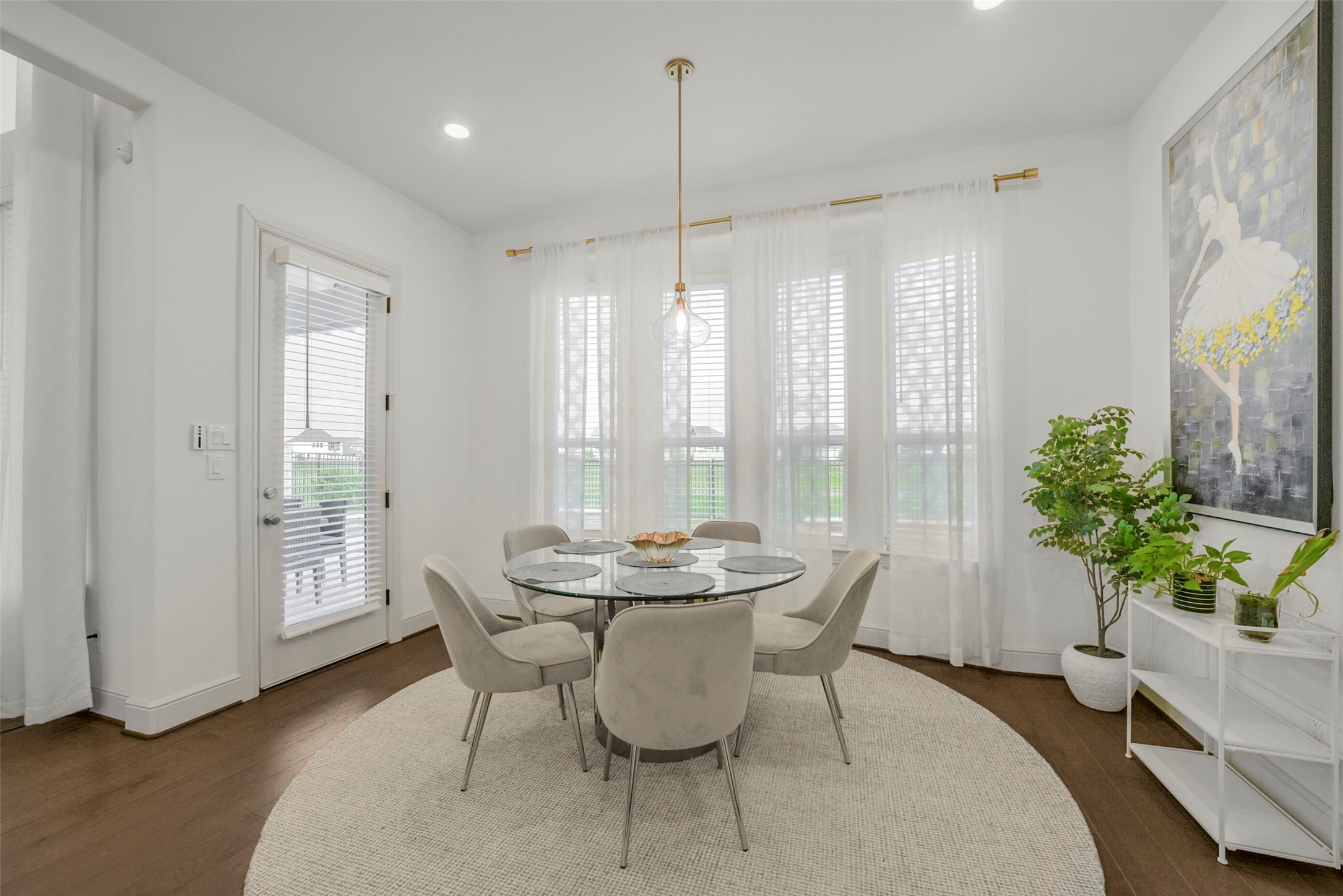 2018 Grove Terrace Lane Manvel, TX 77578 - Photo 15 of 50 Bright dining area with a modern glass table and cushioned chairs on a neutral rug. Large windows with sheer curtains provide ample natural light, and a door leads to an outdoor space. A painting and potted plants add decorative touches.