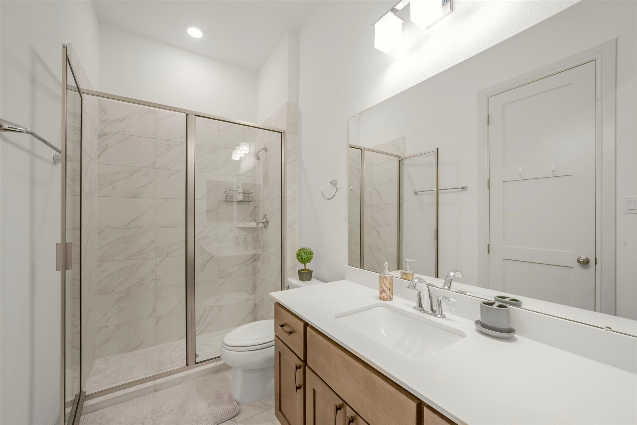 2018 Grove Terrace Lane Manvel, TX 77578 - Photo 19 of 50 This bathroom features a sleek modern design with a spacious glass-enclosed shower, elegant marble tile, a large mirror, and ample storage in a wooden vanity. Bright lighting enhances the clean, fresh look.