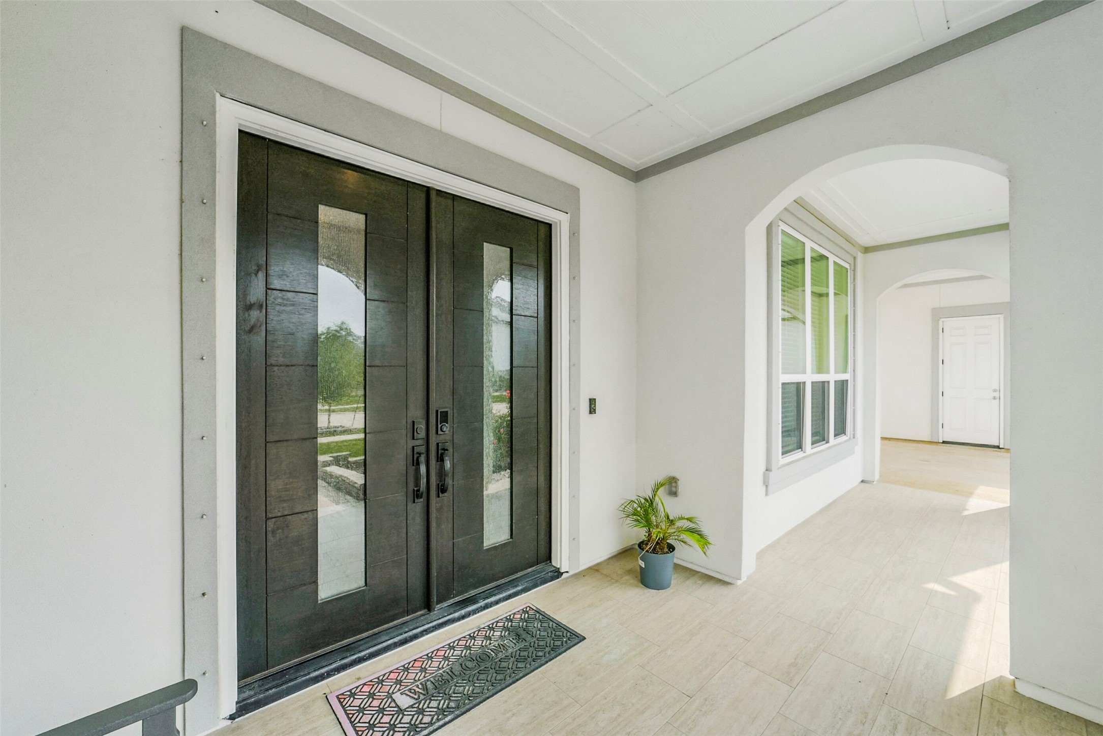 2018 Grove Terrace Lane Manvel, TX 77578 - Photo 2 of 50 Modern entryway with double glass-paneled doors, a light tiled floor, and a small potted plant. The covered porch features an arched window and doorway, providing a welcoming and stylish entrance.