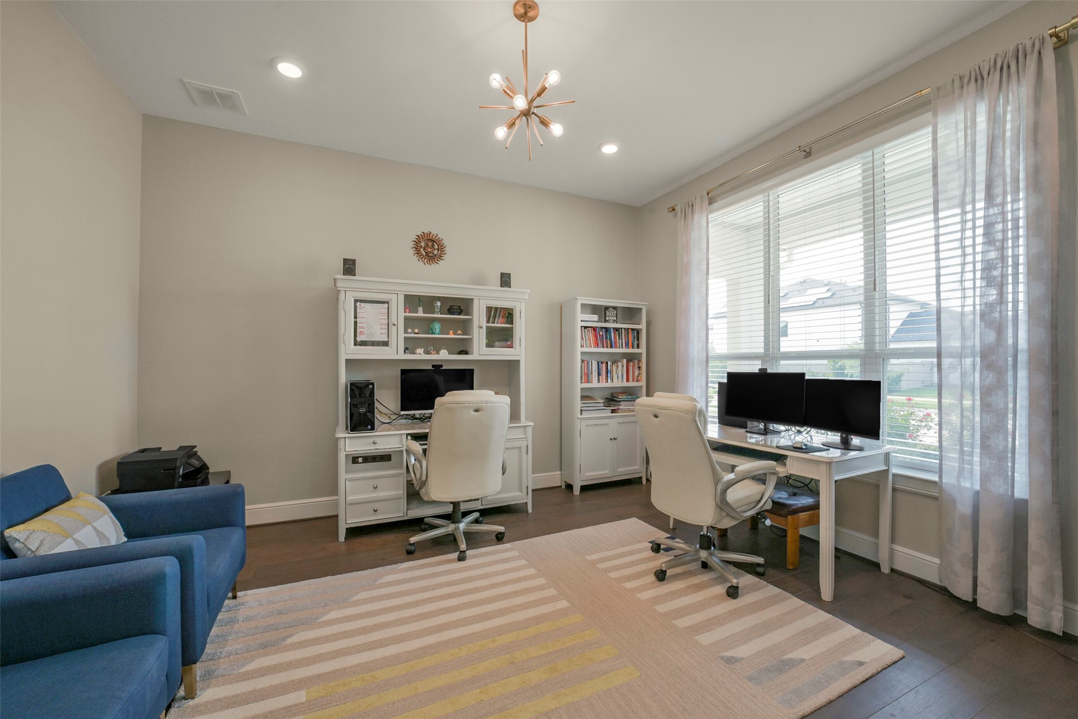 2018 Grove Terrace Lane Manvel, TX 77578 - Photo 21 of 50 This bright home office features large windows with ample natural light, two workstations with white desks and chairs, a cozy blue armchair, and a modern light fixture, creating a functional yet stylish workspace.