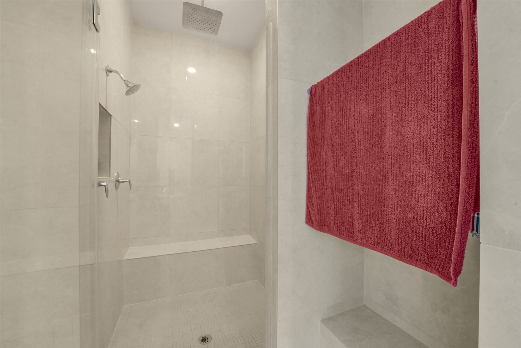2018 Grove Terrace Lane Manvel, TX 77578 - Photo 27 of 50 This bathroom features a modern, spacious custom walk-in shower with sleek tiling, dual showerheads, rain shower and a convenient built-in bench, complemented by a deep red towel for a touch of color.