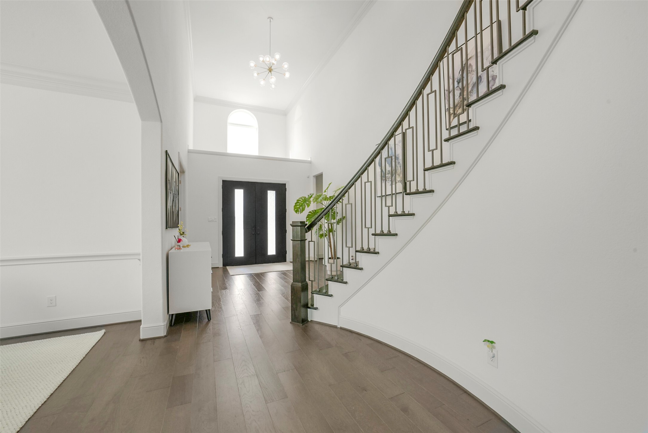 2018 Grove Terrace Lane Manvel, TX 77578 - Photo 28 of 50 Modern, elegant foyer with a high ceiling and a stunning curved wood steps staircase. The space is bright and open, featuring sleek hardwood floors and a contemporary chandelier, creating a welcoming and sophisticated entrance.