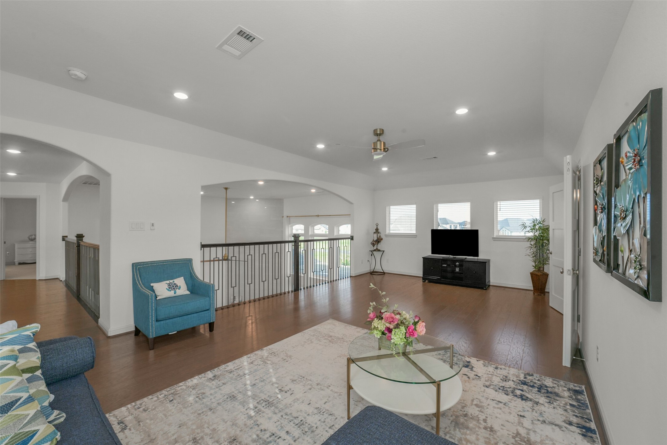 2018 Grove Terrace Lane Manvel, TX 77578 - Photo 30 of 50 This spacious game room living area features hardwood floors, ample natural light from multiple windows, and recessed lighting. Attached built in workstation secondary office. It includes a comfortable seating arrangement, a ceiling fan, and a stylish railing overlooking the lower level. Ideal for relaxation and entertaining.