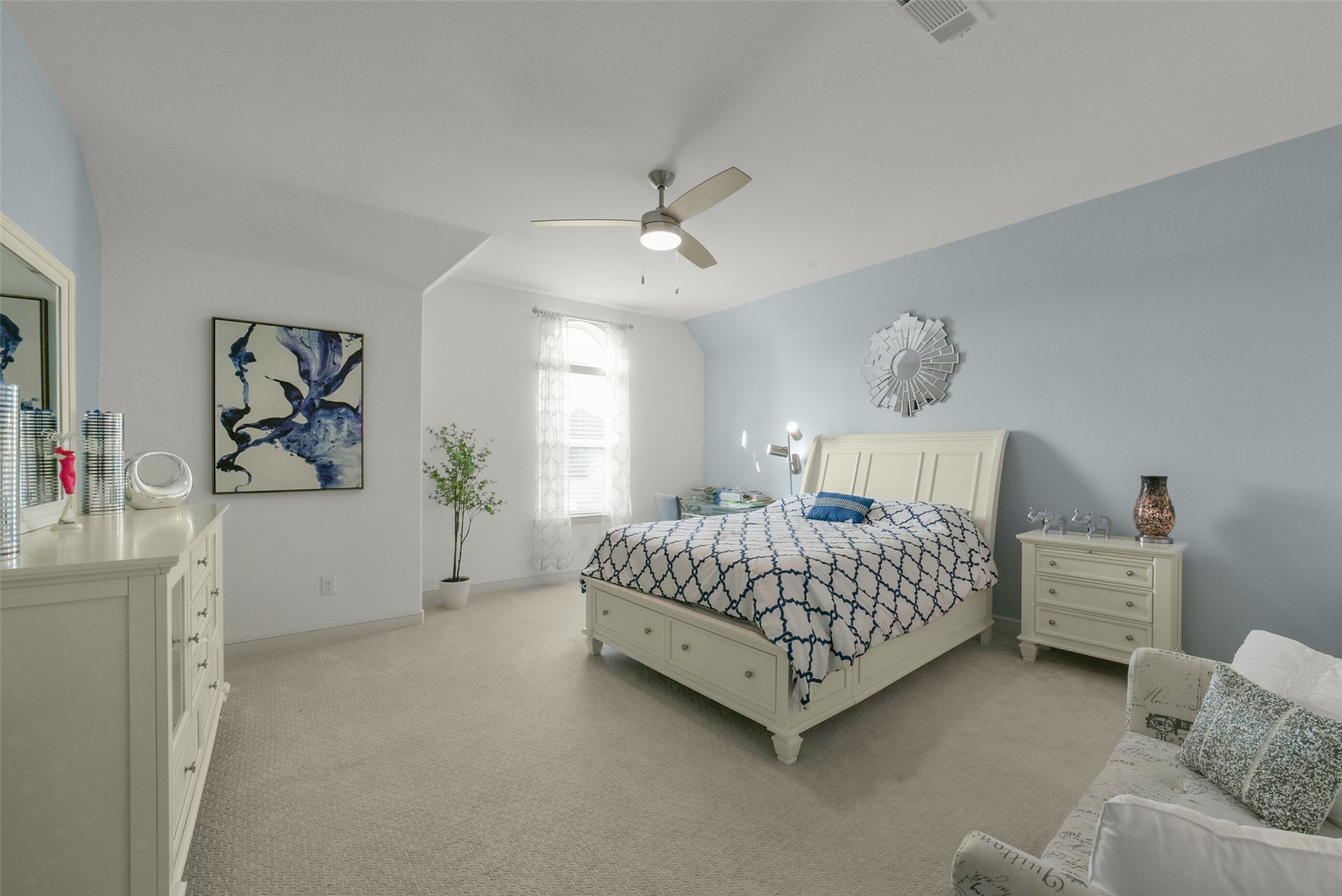2018 Grove Terrace Lane Manvel, TX 77578 - Photo 33 of 50 Spacious secondary bedroom features a soft blue accent wall, a comfortable bed with a patterned duvet, and matching white furniture. It includes a ceiling fan, custom built in closet, decorative artwork, and natural light from a window with sheer curtains, creating a cozy and inviting atmosphere.