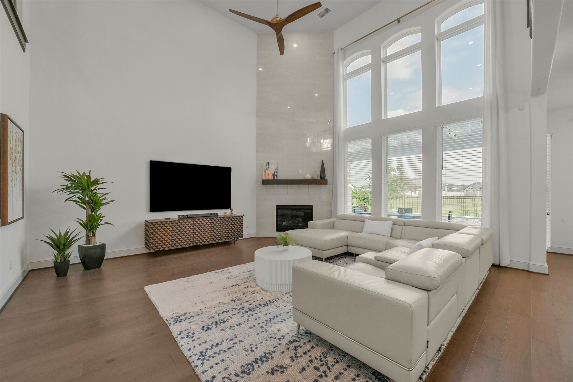 2018 Grove Terrace Lane Manvel, TX 77578 - Photo 4 of 50 This spacious living room features high ceilings and large windows that let in plenty of natural light. It includes a modern fireplace, a mounted TV, and a comfortable sectional sofa. The wood flooring and minimalist decor create a warm, inviting atmosphere.