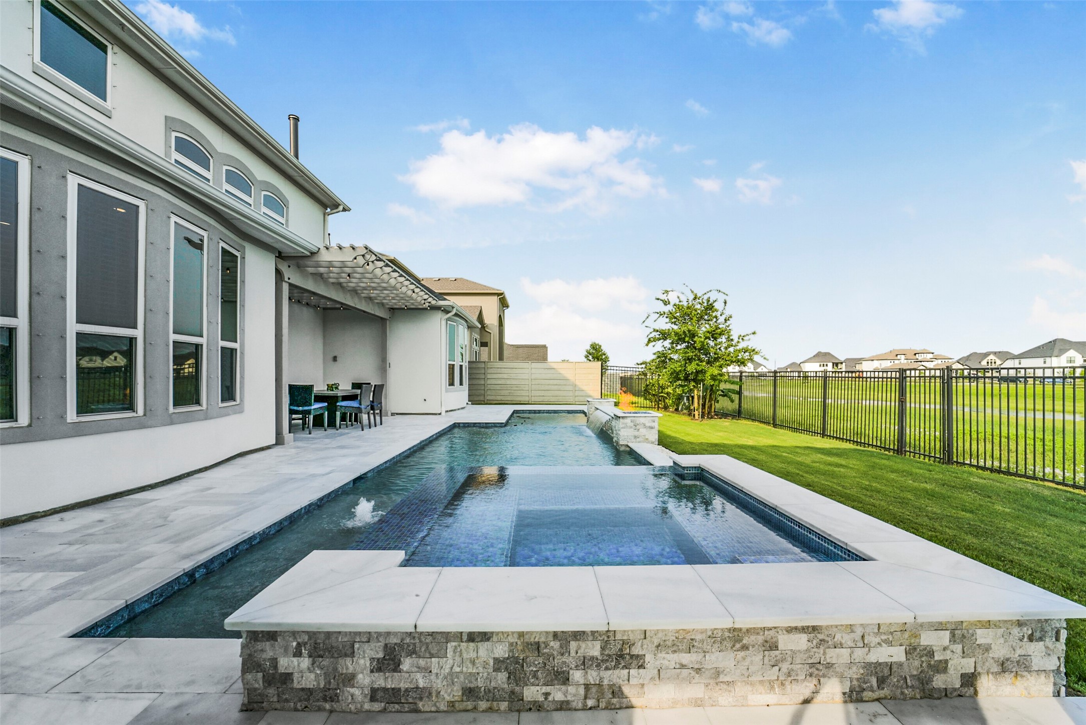 2018 Grove Terrace Lane Manvel, TX 77578 - Photo 42 of 50 Modern home with large windows and a sleek patio area featuring a luxurious in-ground pool. The backyard is iron fenced, offering views of a spacious, open field, providing both privacy and scenic vistas.