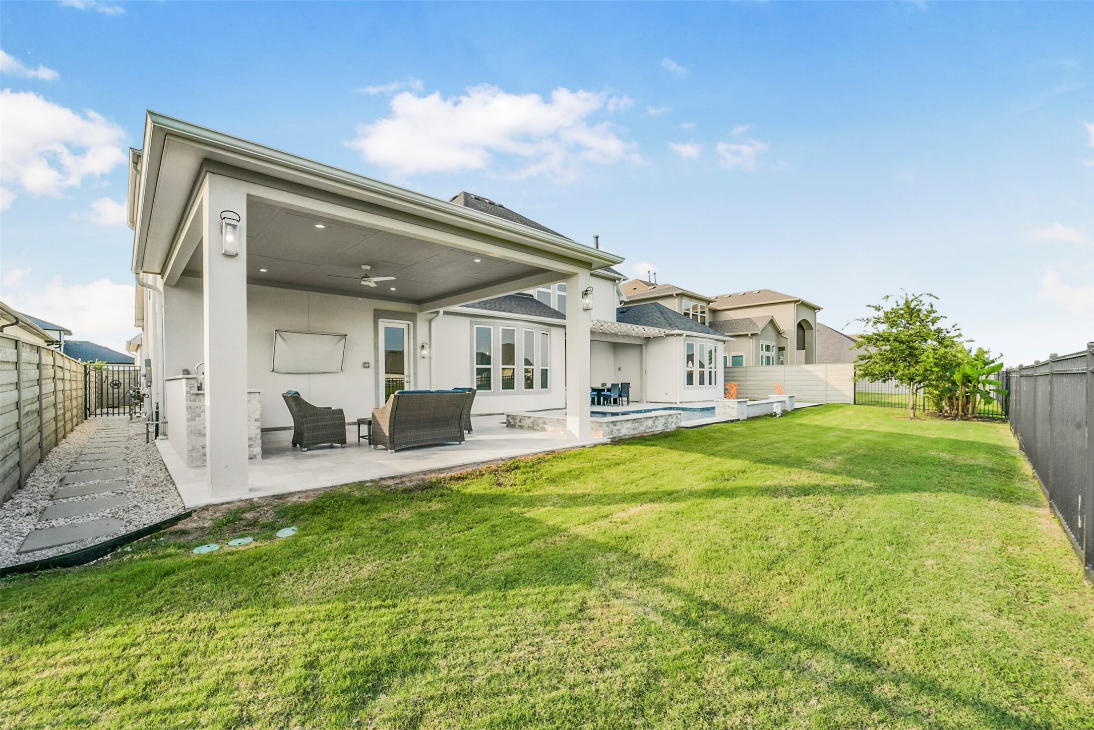 2018 Grove Terrace Lane Manvel, TX 77578 - Photo 45 of 50 Spacious backyard featuring a well-maintained lawn and a covered patio with seating and outdoor kitchen. The area is perfect for outdoor relaxation and entertaining. The house has a modern exterior with large windows, enhancing the natural light inside.