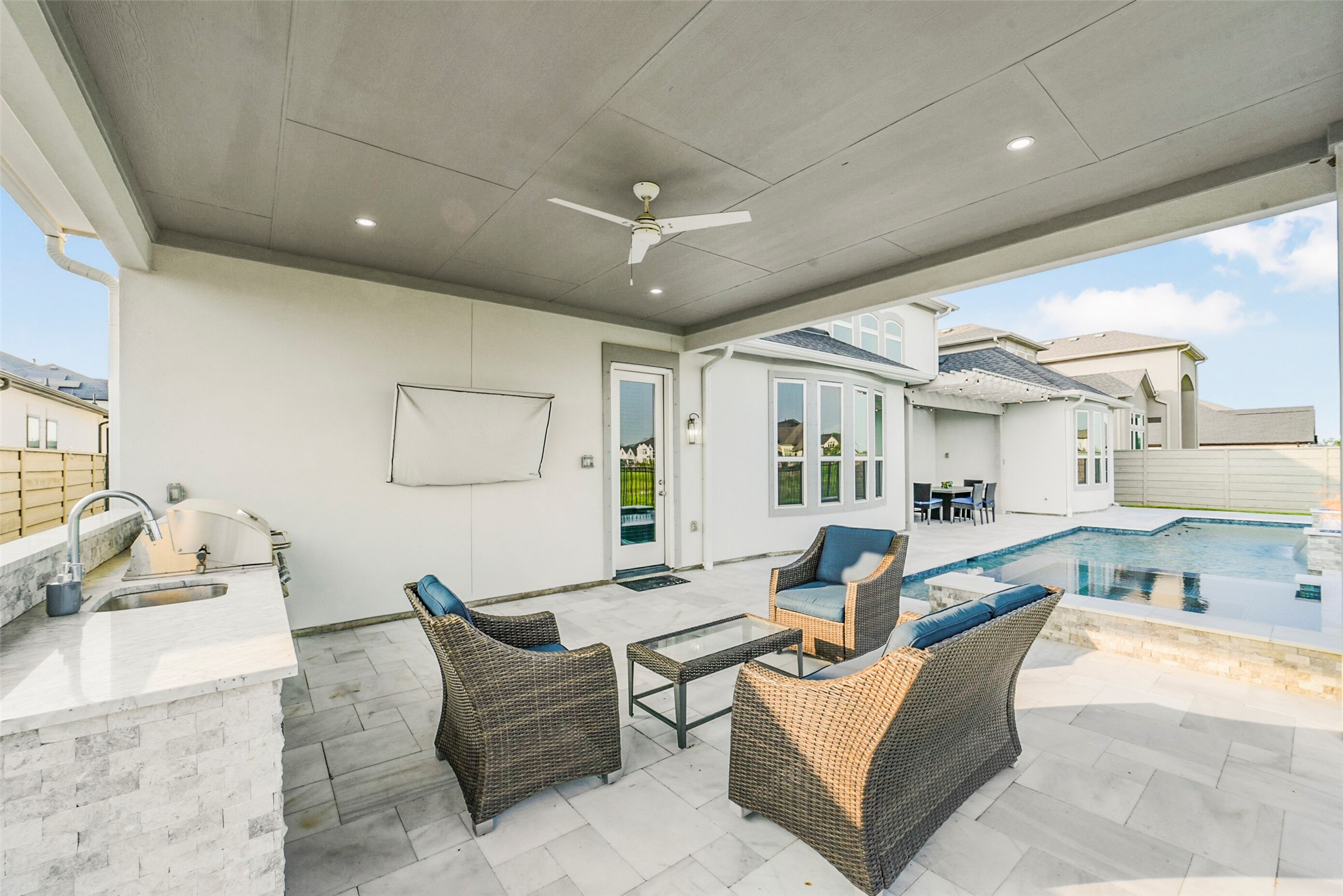 2018 Grove Terrace Lane Manvel, TX 77578 - Photo 46 of 50 Modern outdoor living space with a covered patio featuring wicker seating, a ceiling fan, and a built-in kitchenette. Overlooking a sleek pool, it's perfect for relaxation and entertaining.