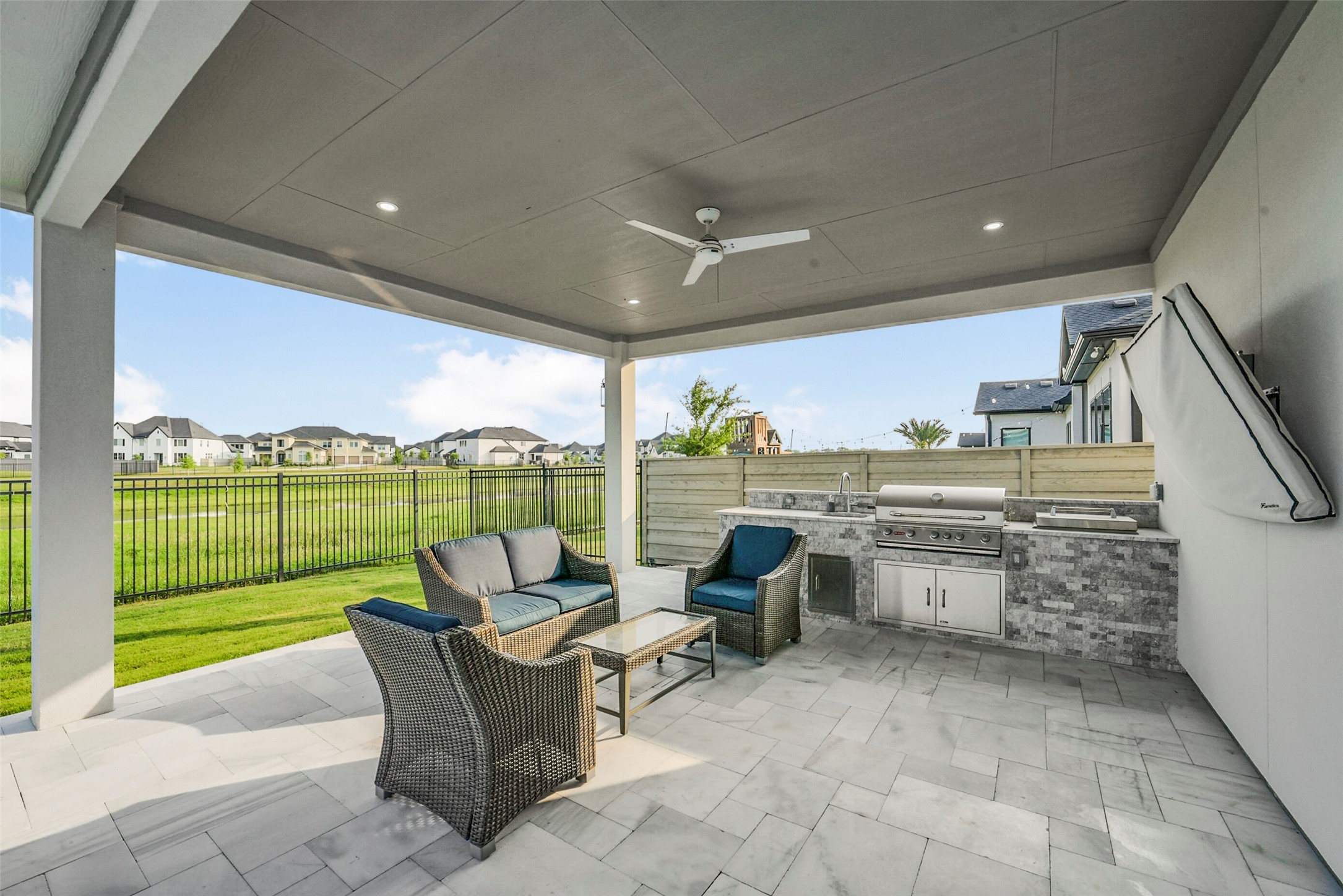 2018 Grove Terrace Lane Manvel, TX 77578 - Photo 47 of 50 Outdoor patio features a covered seating area with modern wicker furniture, a built-in stainless steel grill, and a ceiling fan, overlooking a fenced, landscaped yard. Perfect for entertaining and relaxing.