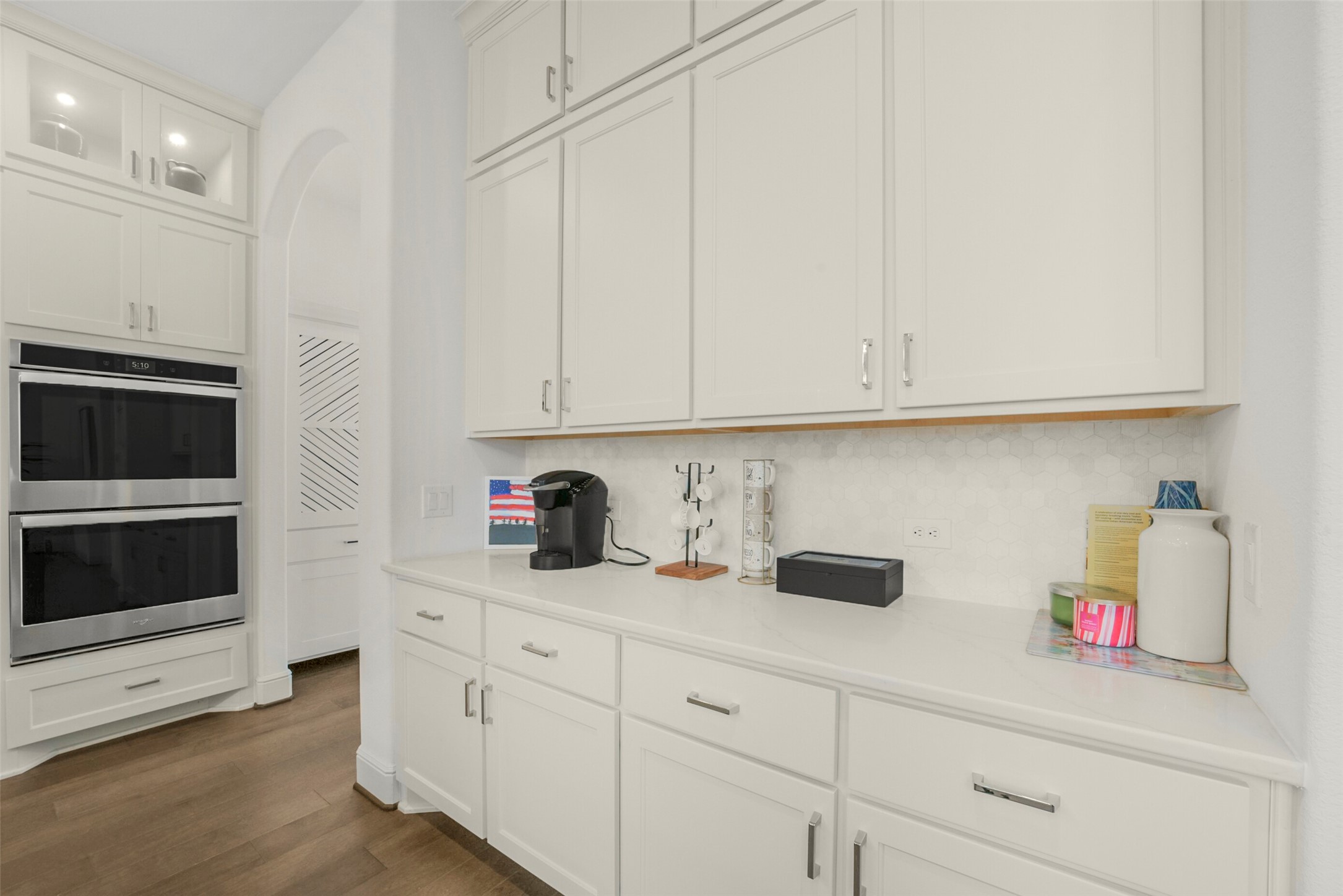 2018 Grove Terrace Lane Manvel, TX 77578 - Photo 9 of 50 This kitchen features sleek white cabinetry with ample storage, a built-in double oven, and a convenient coffee station on the counter. The light wood flooring and hexagonal tile backsplash add a modern touch.