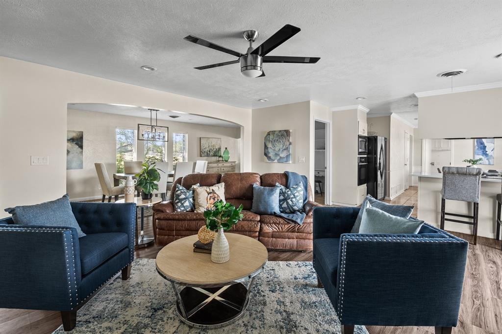 Living room featuring light wood-style flooring, a textured ceiling, arched walkways, ceiling fan, and ornamental molding