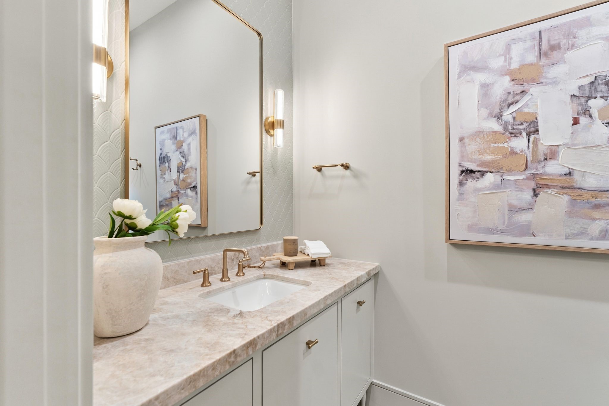 Soft scalloped tile adds texture to this elegant first-floor bathroom, pairing beautifully with a natural stone countertop and champagne gold hardware. Hinkley Georgette sconces in lacquered brass frame the mirror, while a Delta Saylor faucet completes the vanity.