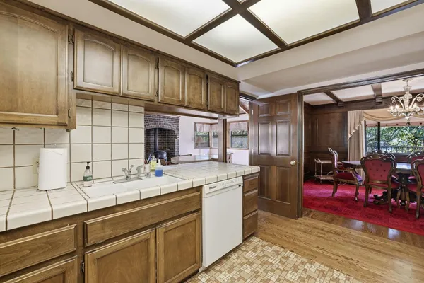 a kitchen with a sink dishwasher a stove and chairs with wooden floor